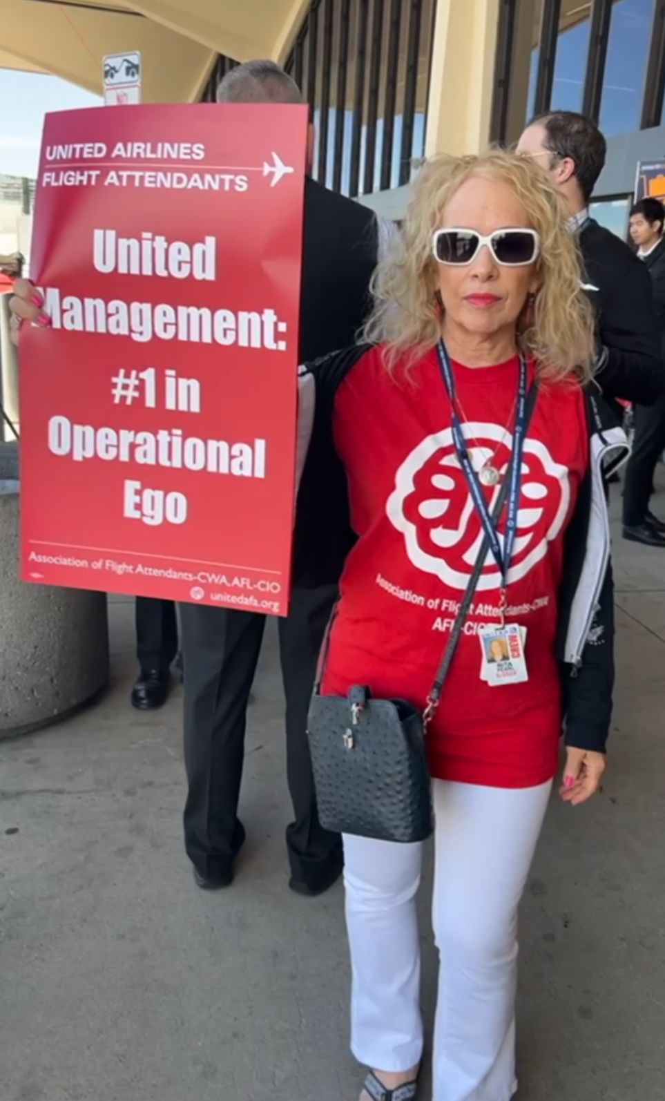 Rita Pearl holding a sign that reads 'United Management: #1 in Operational Ego'.